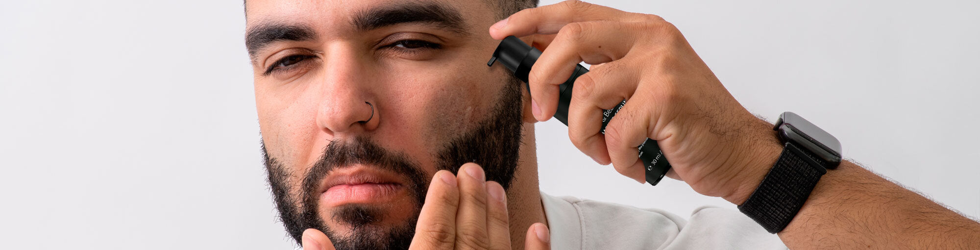 Wide banner of a man aplying beard serum on his long hair beard on his face.