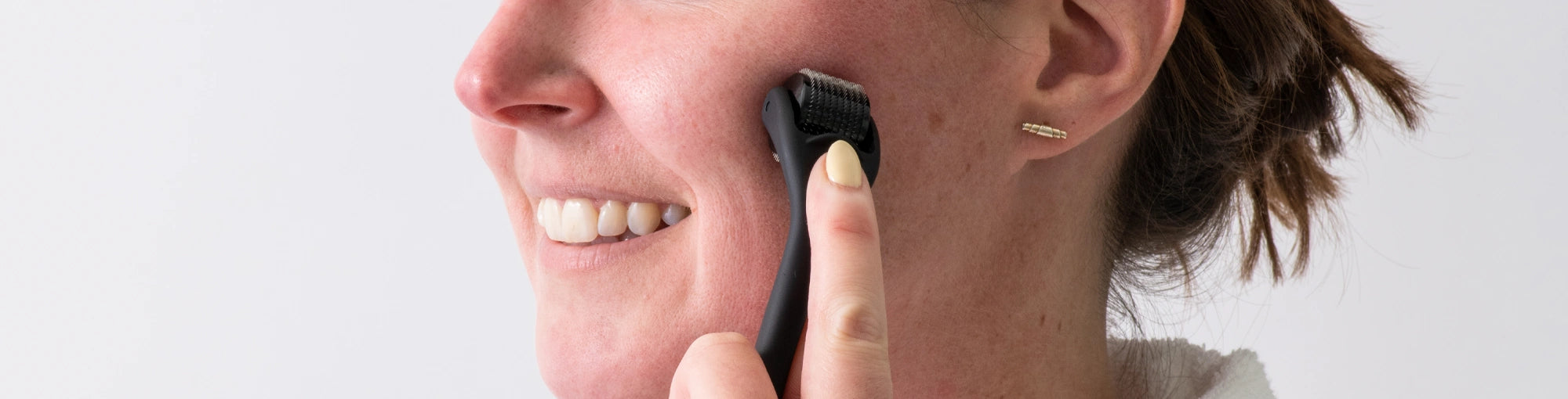 Woman applying a derma roller to her face for skin rejuvenation, collagen production, and improved absorption of skincare products. Explore the benefits of at-home microneedling with DermTechRoller.