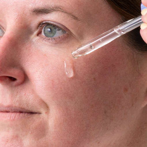 Woman using a dropper to apply hydrating serum or oil to her face for improved skin hydration and rejuvenation. Discover the benefits of microneedling and skincare routines with DermTechRoller.